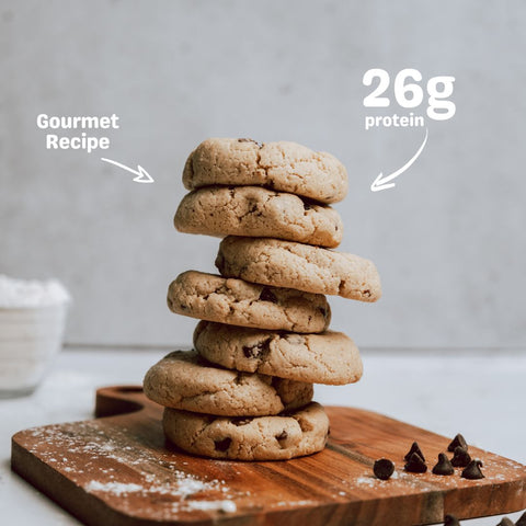 Stack of ChunkyFit Classic Chocolate Chip Protein Cookies on a wooden board, with a label highlighting 26g of protein per cookie.